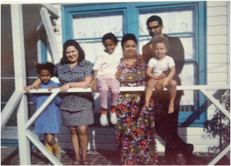 Old image of family at a house railing, three adults and 3 young children.